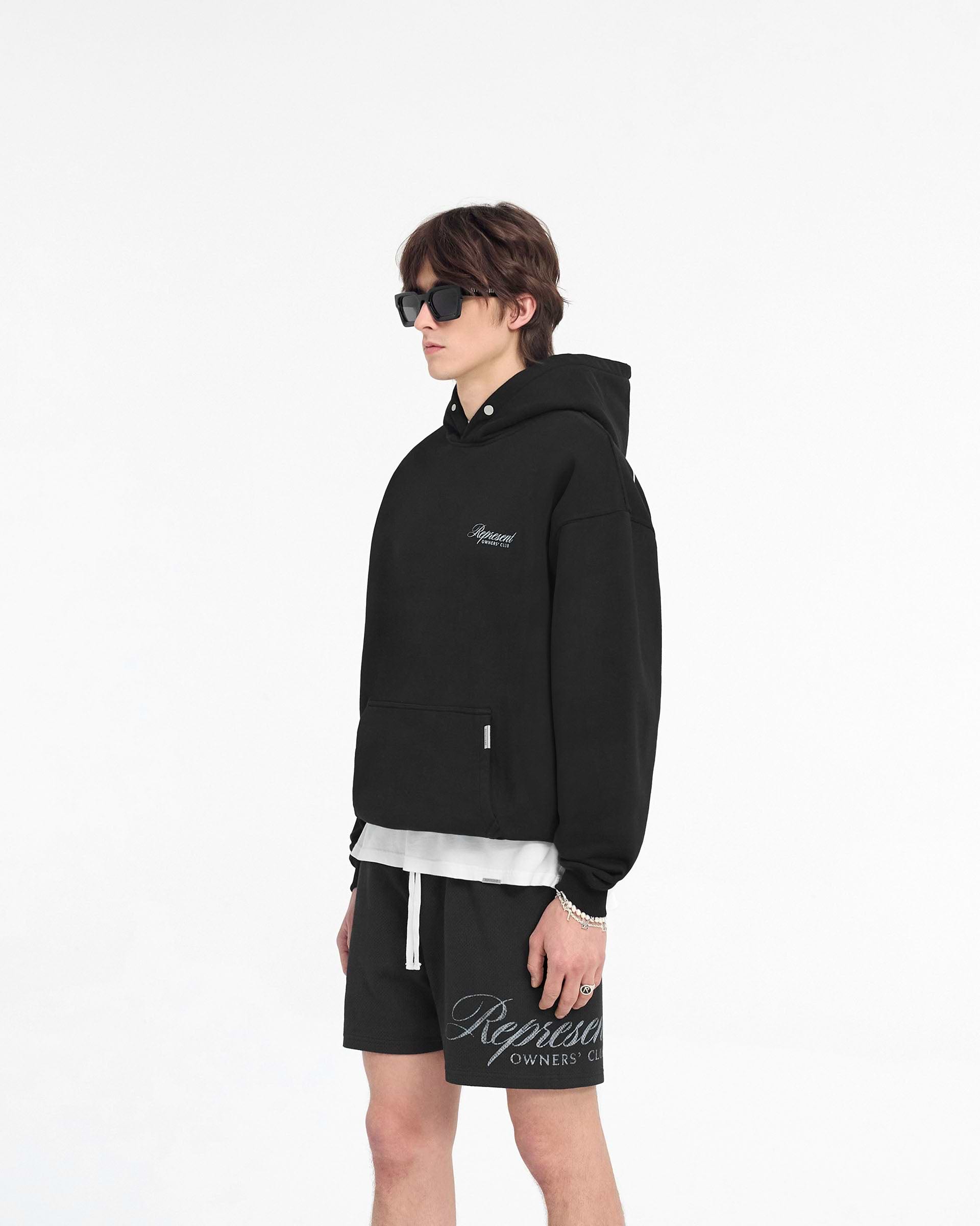Man wearing a black hoodie on a plain white background | Represent Owners Club Script Hoodie in Black | Heavy weight hoodie with ribbed trims and script graphic | Owners Club Hoodies | Represent Clo