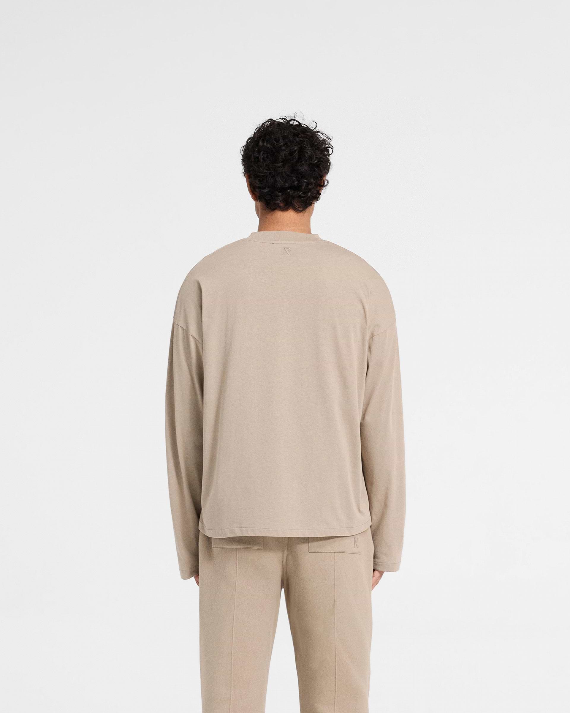 Man wearing an oversized dune long sleeve t-shirt on a plain white background | Initial Long Sleeve Open Cuff T-Shirt in Dune | Boxy fit with open cuffs | Initial T-Shirts | Represent Clo