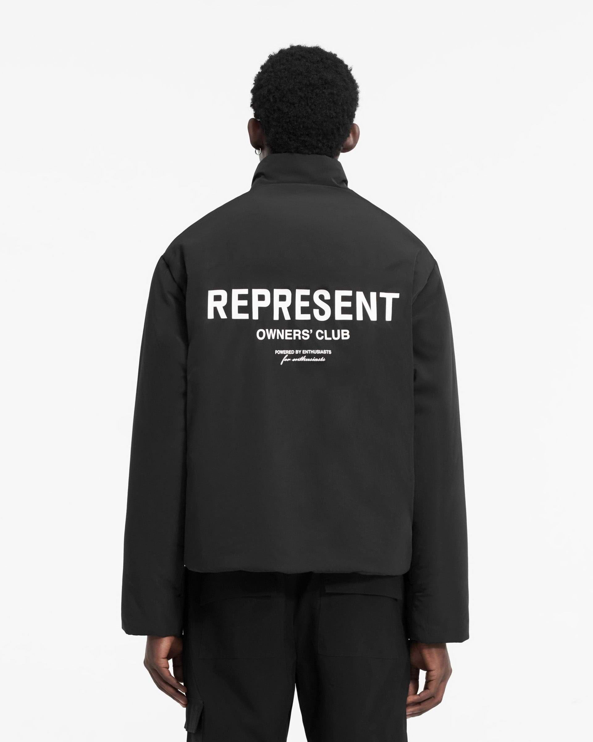 Man wearing a black down-filled jacket on a plain white background | Owners Club Wadded Jacket in Black | Wadded jacket with zip closure and pockets | Owners Club Outerwear | Represent Clo