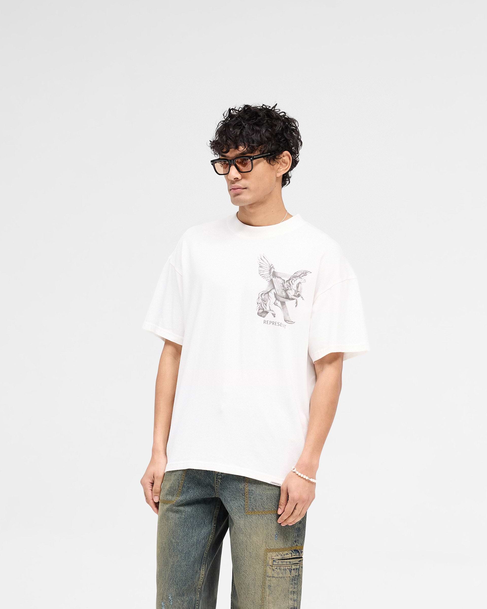 Man wearing a white graphic t-shirt on a plain white background | Elegance In Motion T-Shirt in Flat White | Oversized t-shirt with graphic and metal bar logo | SS25 T-Shirts | Represent Clo