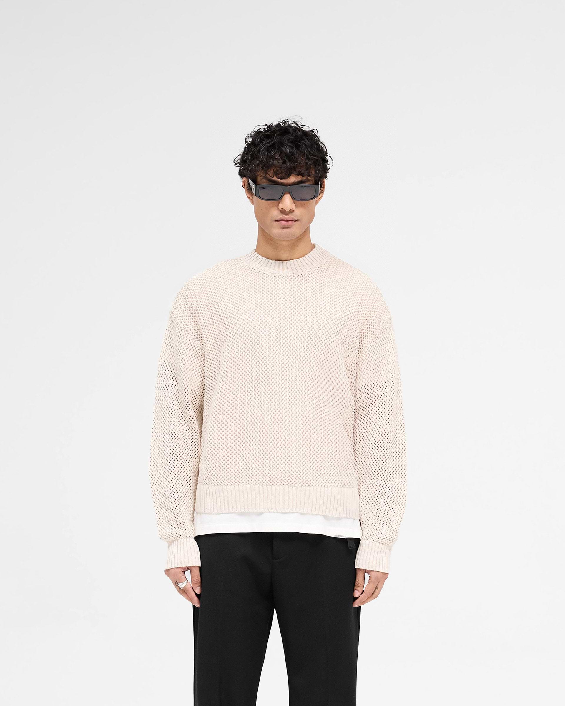 Man wearing an off-white knit sweater on a plain white background | Open Gauge Knit Sweater in Off White | Slightly oversized knitwear with ribbed detailing | SS25 Knitwear | Represent Clo