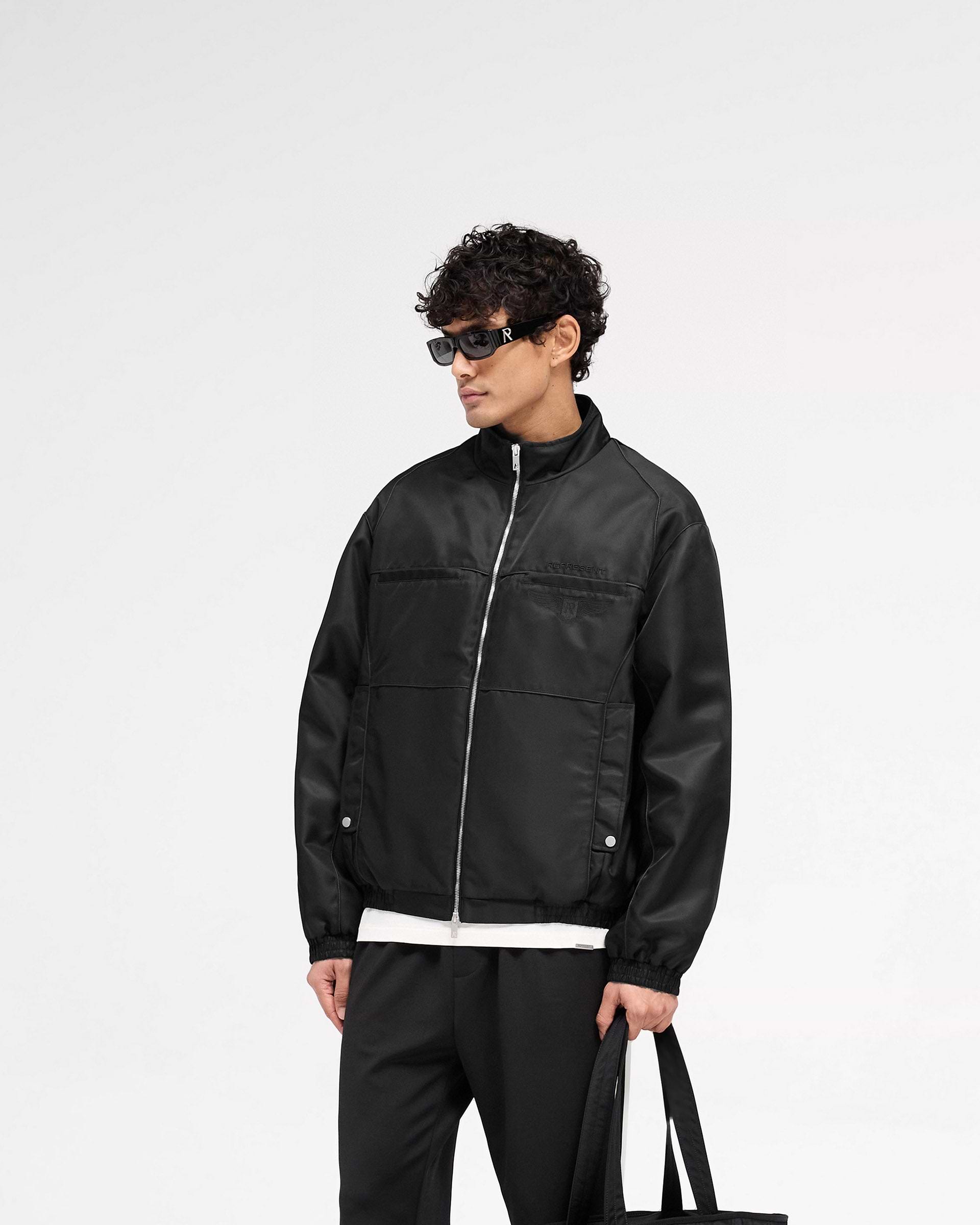 Man wearing an oversized black jacket on a plain white background | Overdrive Racing Jacket in Black | Racing jacket with funnel neck and double ended zipper | SS25 Outerwear | Represent Clo