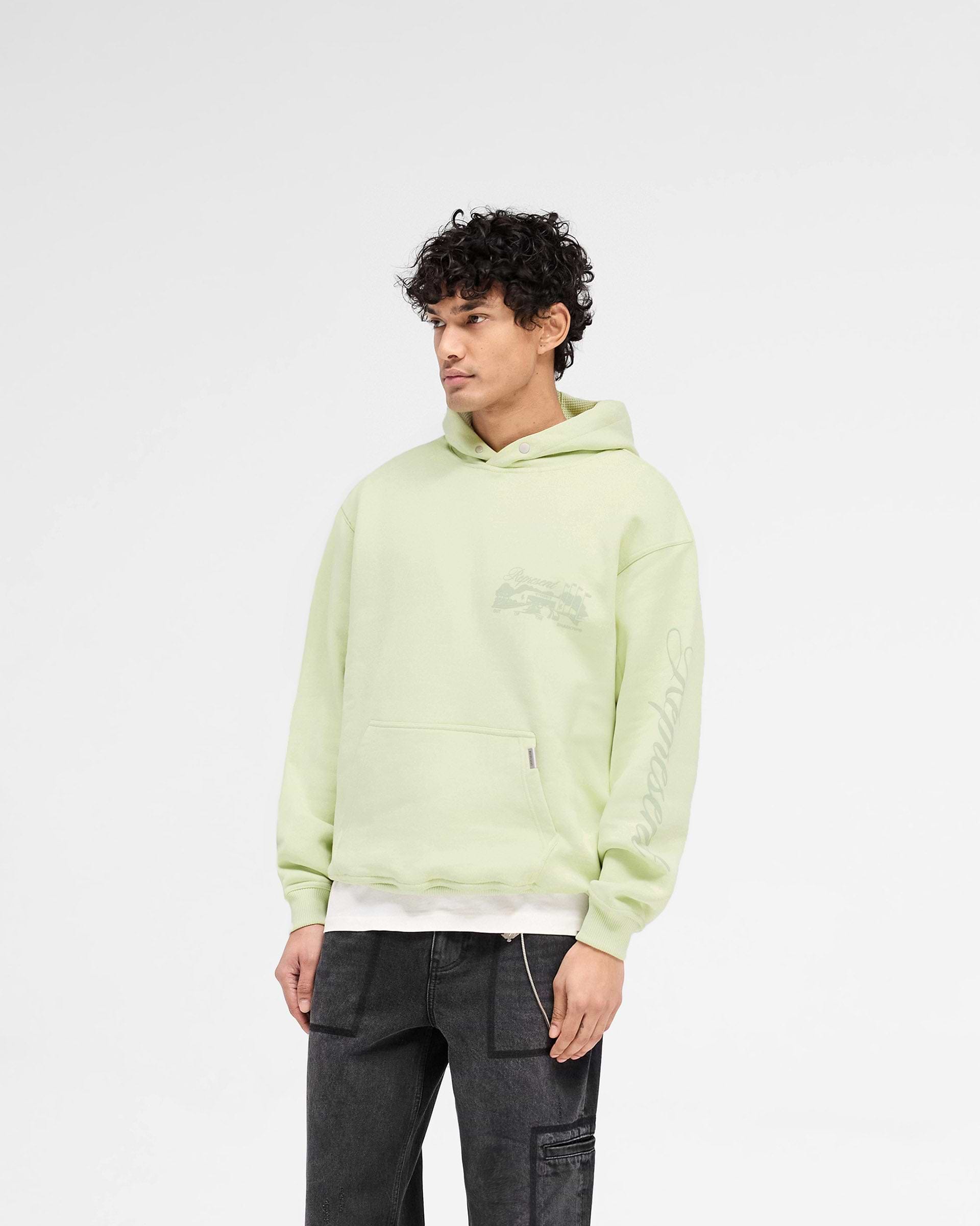 Man wearing a green hoodie on a plain white background | Raceway Hoodie in Matcha | Slightly oversized hoodie with puff print and sleeve detail | SS25 Hoodies | Represent Clo