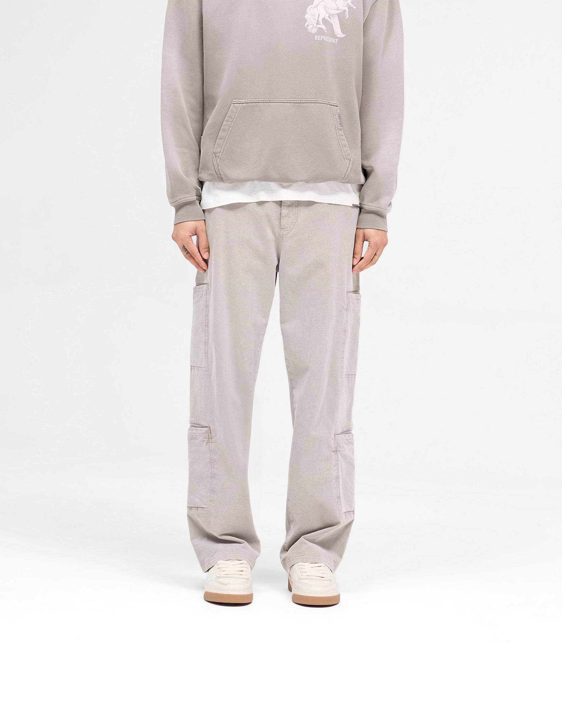 Man wearing beige pants on a plain white background | Season Cargo Pant in Washed Taupe | Cargo pants with brushed twill fabric and eight pockets | SS25 Pants | Represent Clo