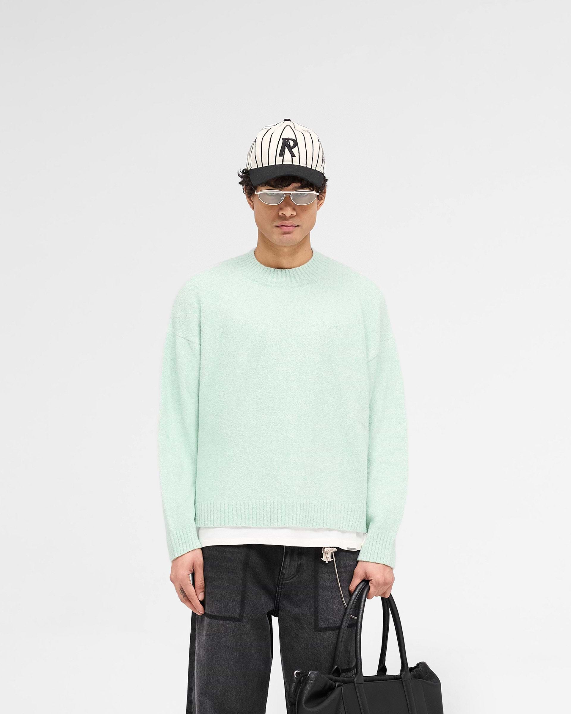 Man wearing a green knit jumper on a plain white background | Marled Knit Jumper in Matcha | Oversized fit knitwear with tonal script embroidery | SS25 Knitwear | Represent Clo