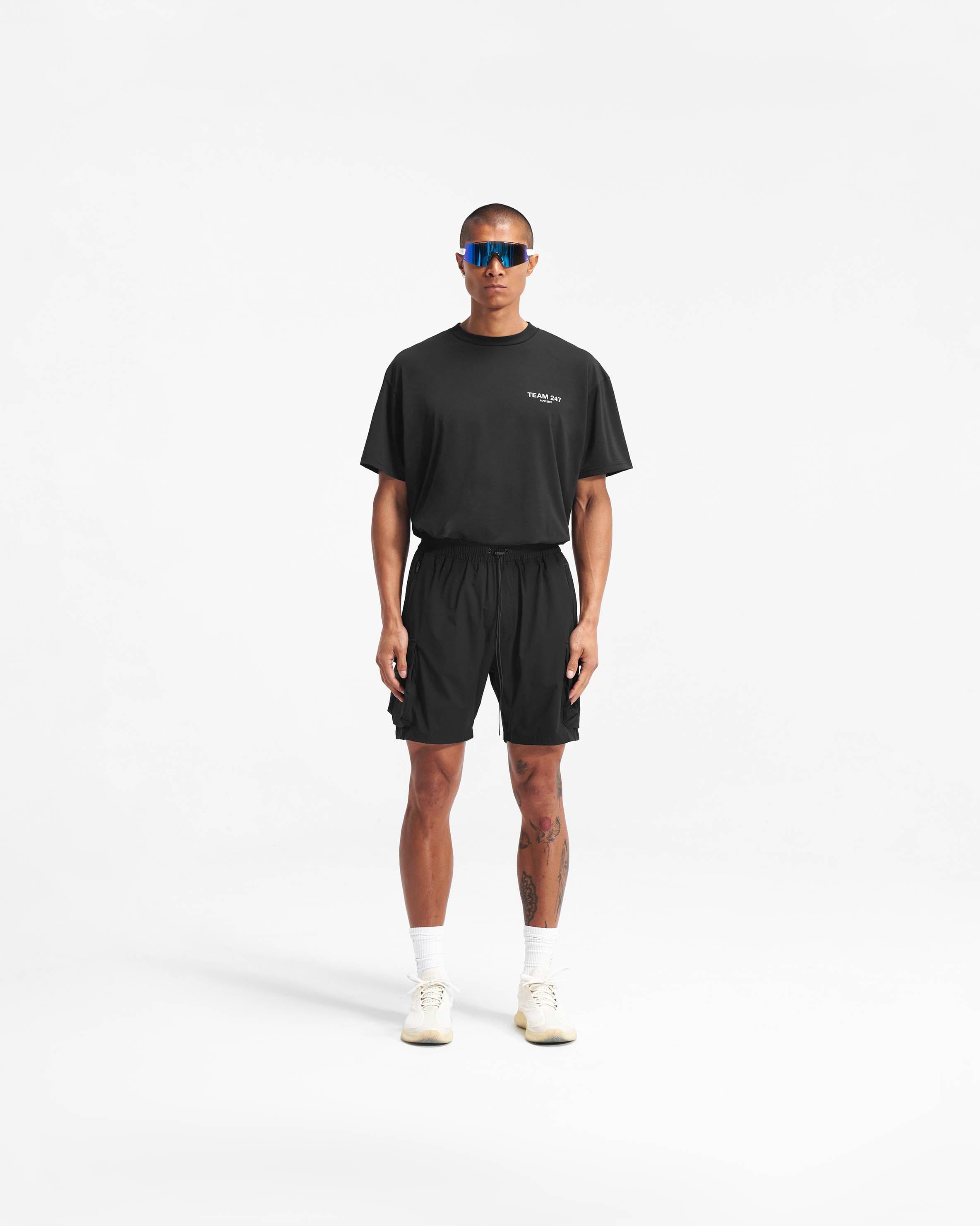 Man wearing black shorts on a plain white background | 247 Shorts in Black | Mens combat shorts with cargo and zip pockets | 247 Shorts | Represent Clo