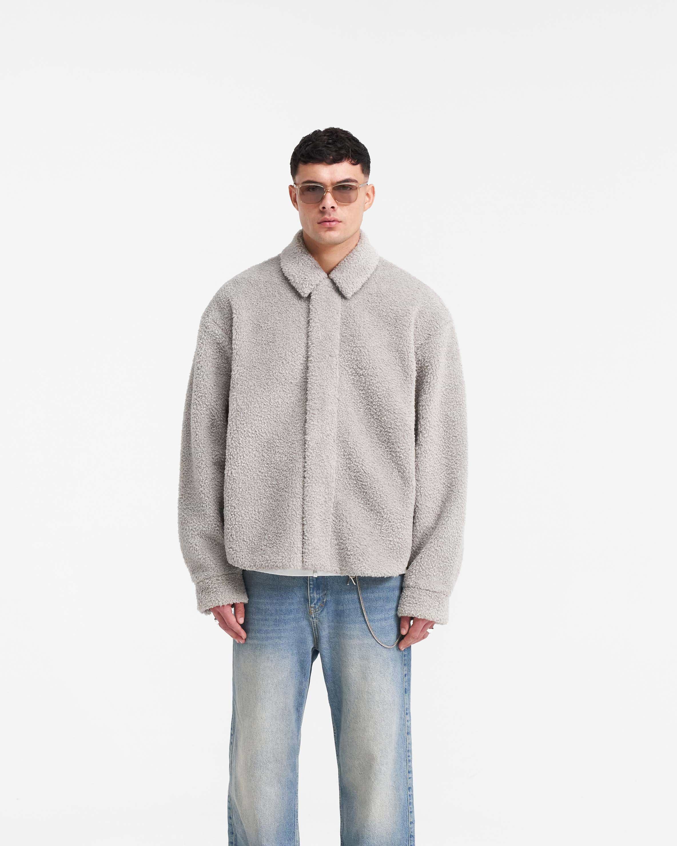 Man wearing a grey shearling shirt on a plain white background | Shearling Scoop Hem Shirt in Ice Grey | Shearling shirt with zip front and adjustable cuffs | PRE SS24 Shirts | Represent Clo