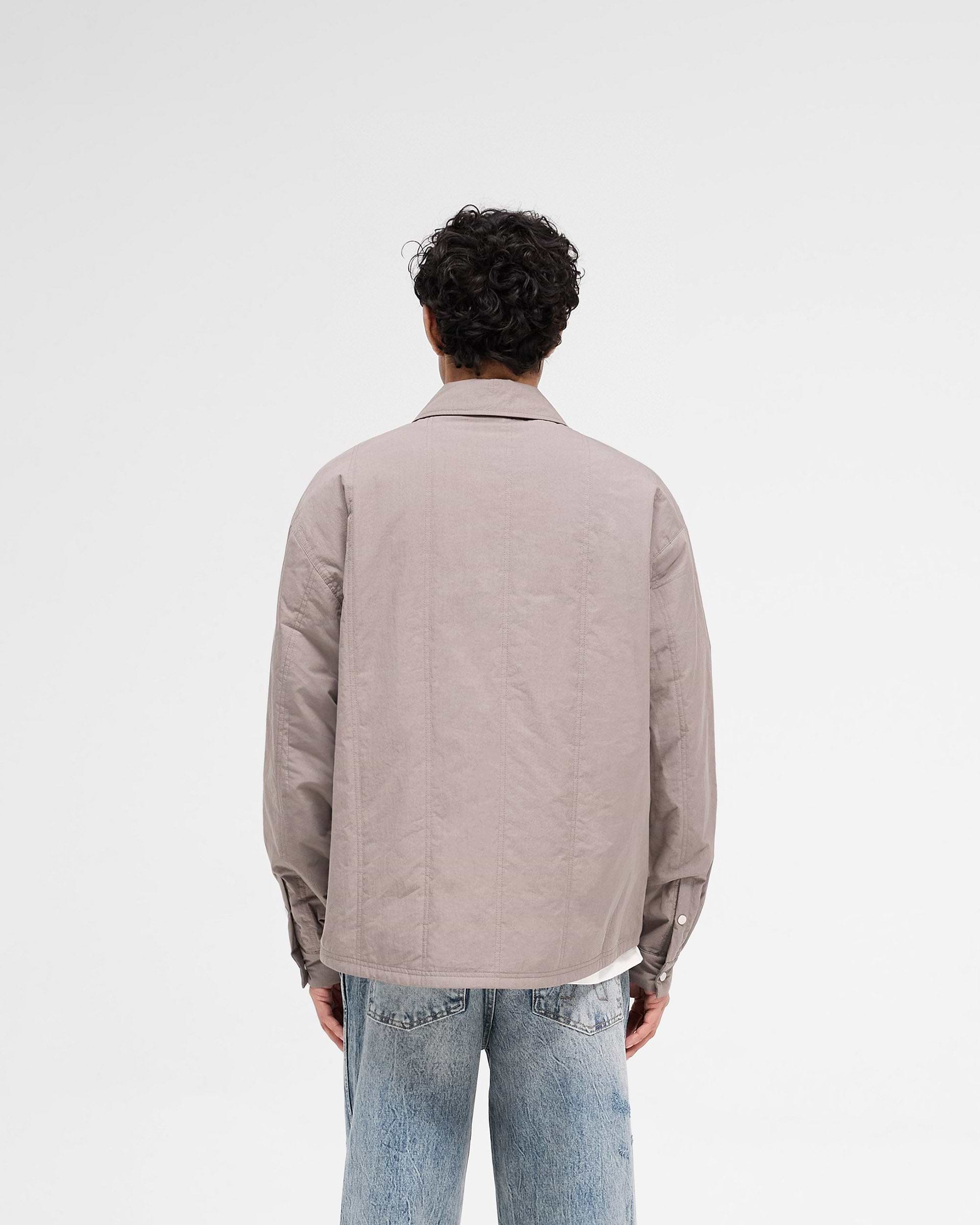 Man wearing a grey quilted overshirt on a plain white background | Quilted Overshirt in Mid Grey | Shirts with twin needle quilting stitches and chest pockets | SS25 Shirts | Represent Clo
