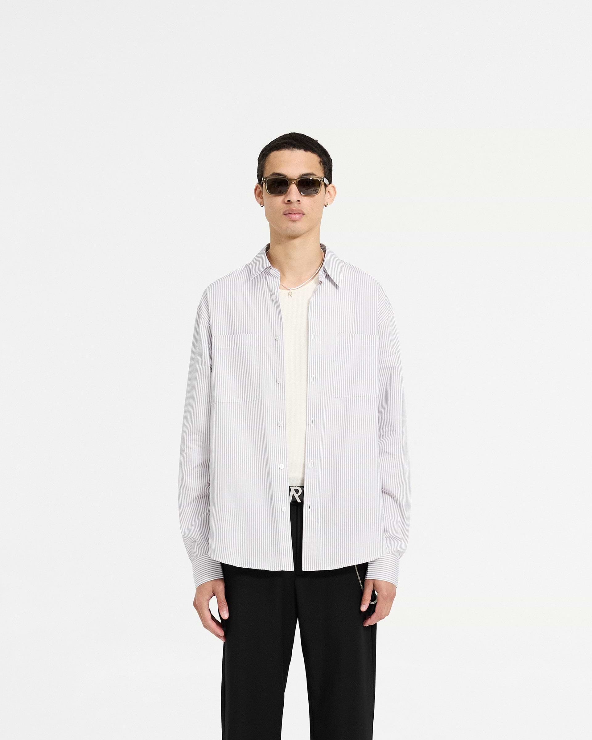 Man wearing a grey pinstripe long sleeve shirt on a plain white background | Long Sleeve Pinstripe Shirt in Grey | Oversized shirt with curved hem and chest pockets | SC24 Shirts | Represent Clo
