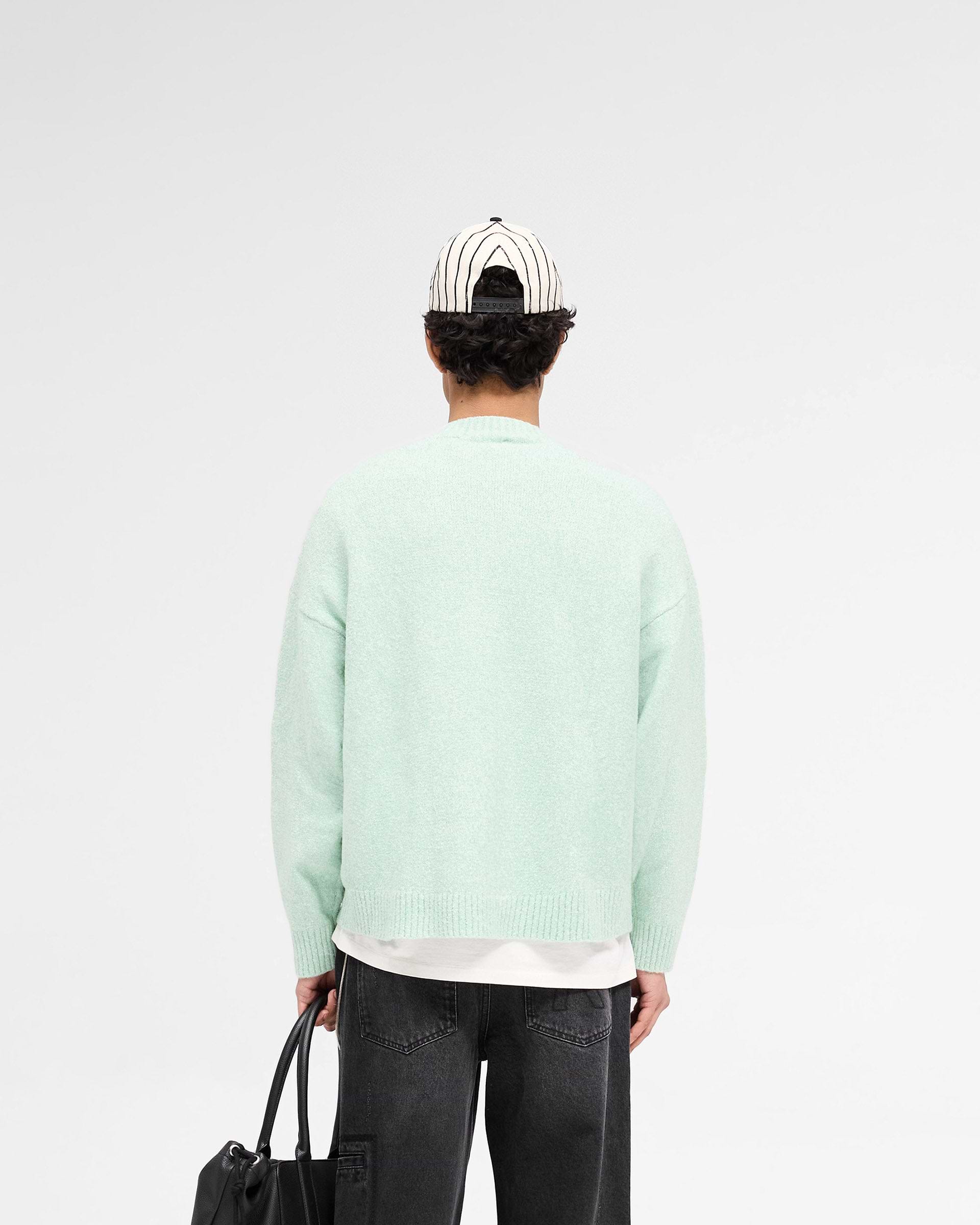 Man wearing a green knit jumper on a plain white background | Marled Knit Jumper in Matcha | Oversized knit jumper with tonal script embroidery | SS25 Knitwear | Represent Clo