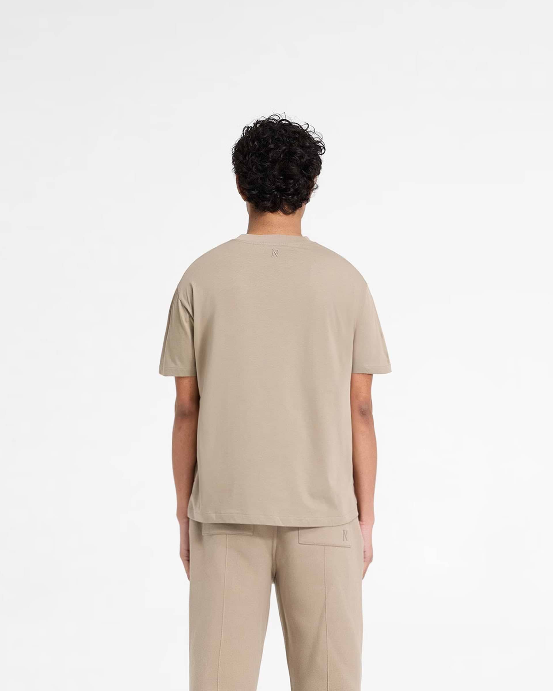 Man wearing a dune t-shirt on a plain white background | Initial T-Shirt in Dune | Slim fit mens t-shirt with embroidered details | Initial T-Shirts | Represent Clo