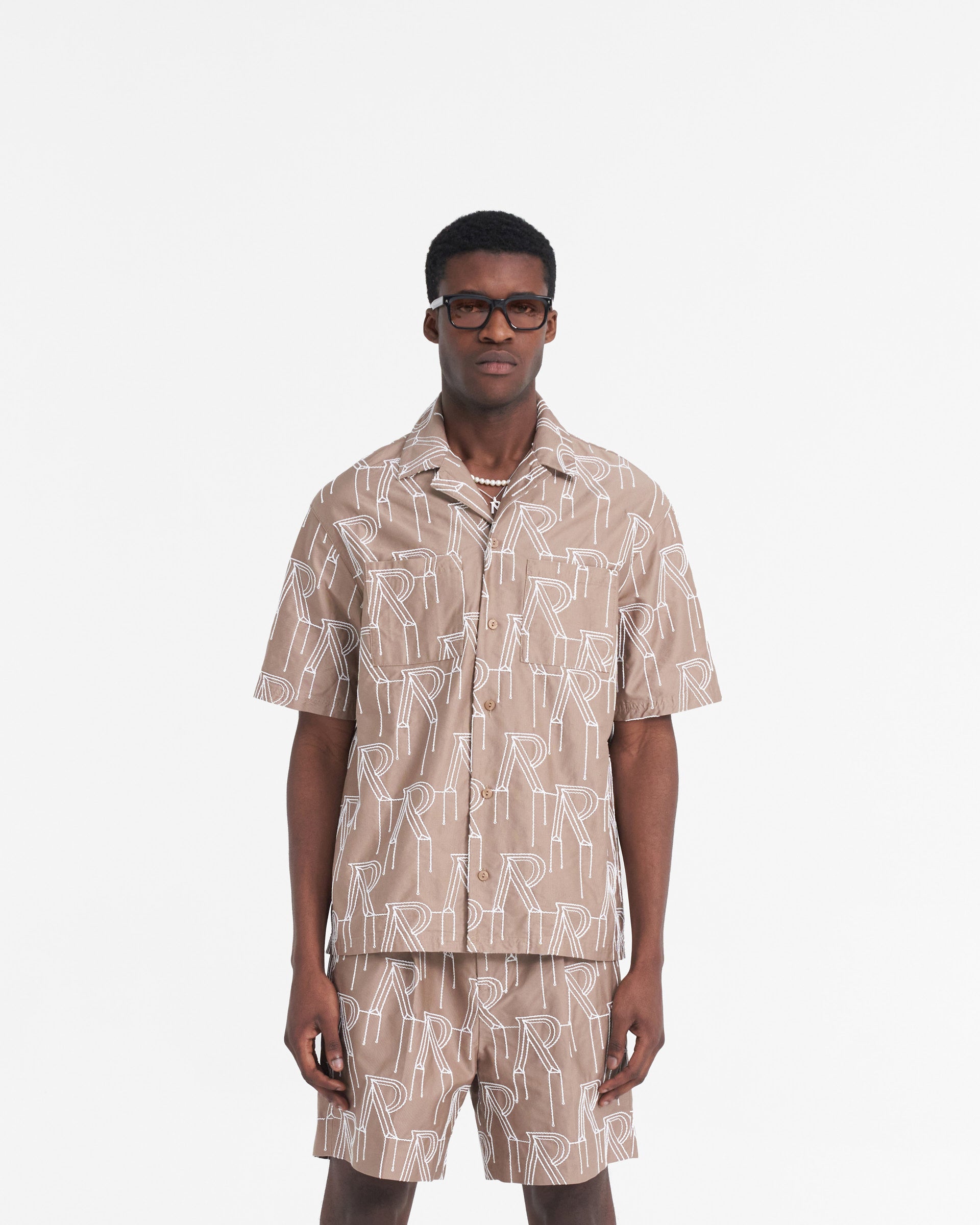 Man wearing an oversized taupe overshirt on a plain white background | Embroidered Initial Overshirt in Washed Taupe | Oversized shirt with chain stitch embroidery and revere collar | SS24 Shirts | Represent Clo
