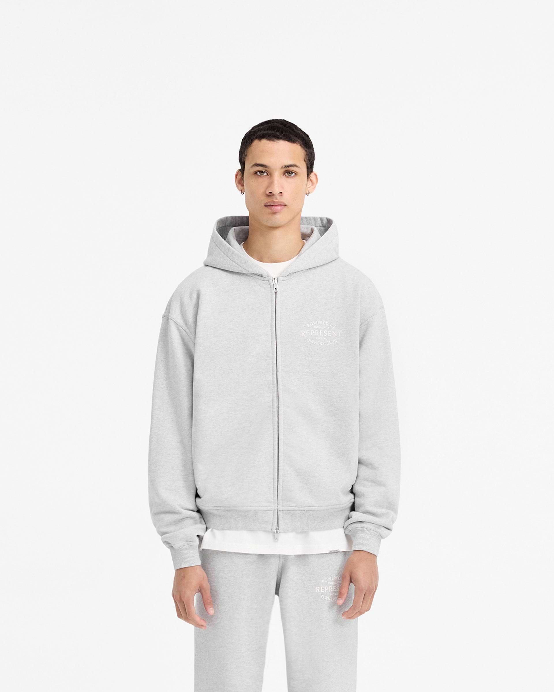 Man wearing an ash grey zip-up hoodie on a plain white background | Represent Owners Club Stamp Zip Up Hoodie in Ash Grey | Heavy weight jersey cotton hoodie with RiRi double ended zip and high build branding | Owners Club Hoodies | Represent Clo