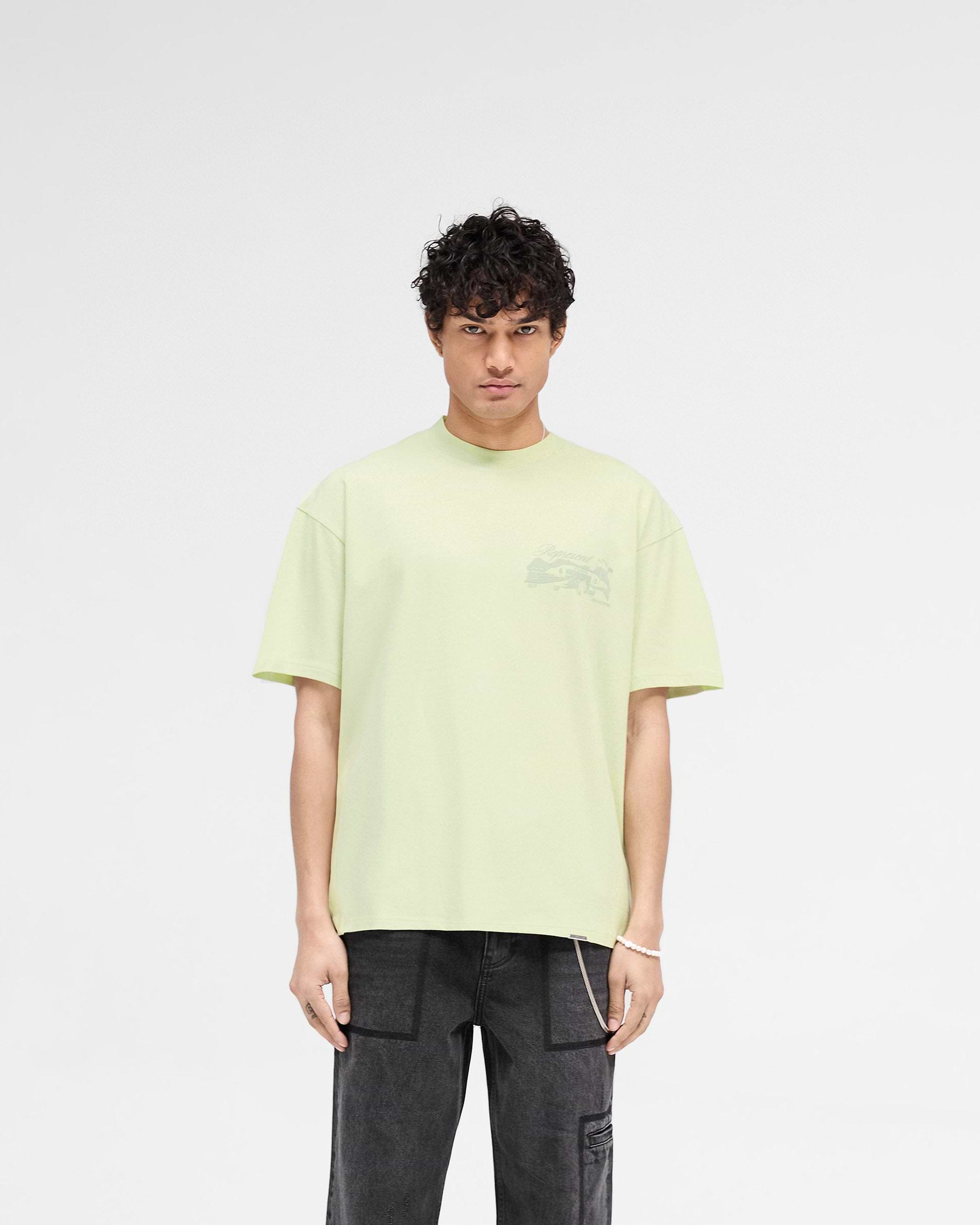 Man wearing a green slightly oversized t-shirt on a plain white background | Raceway T-Shirt in Matcha | T-Shirt with puff print graphic and metal bar logo | SS25 T-Shirts | Represent Clo