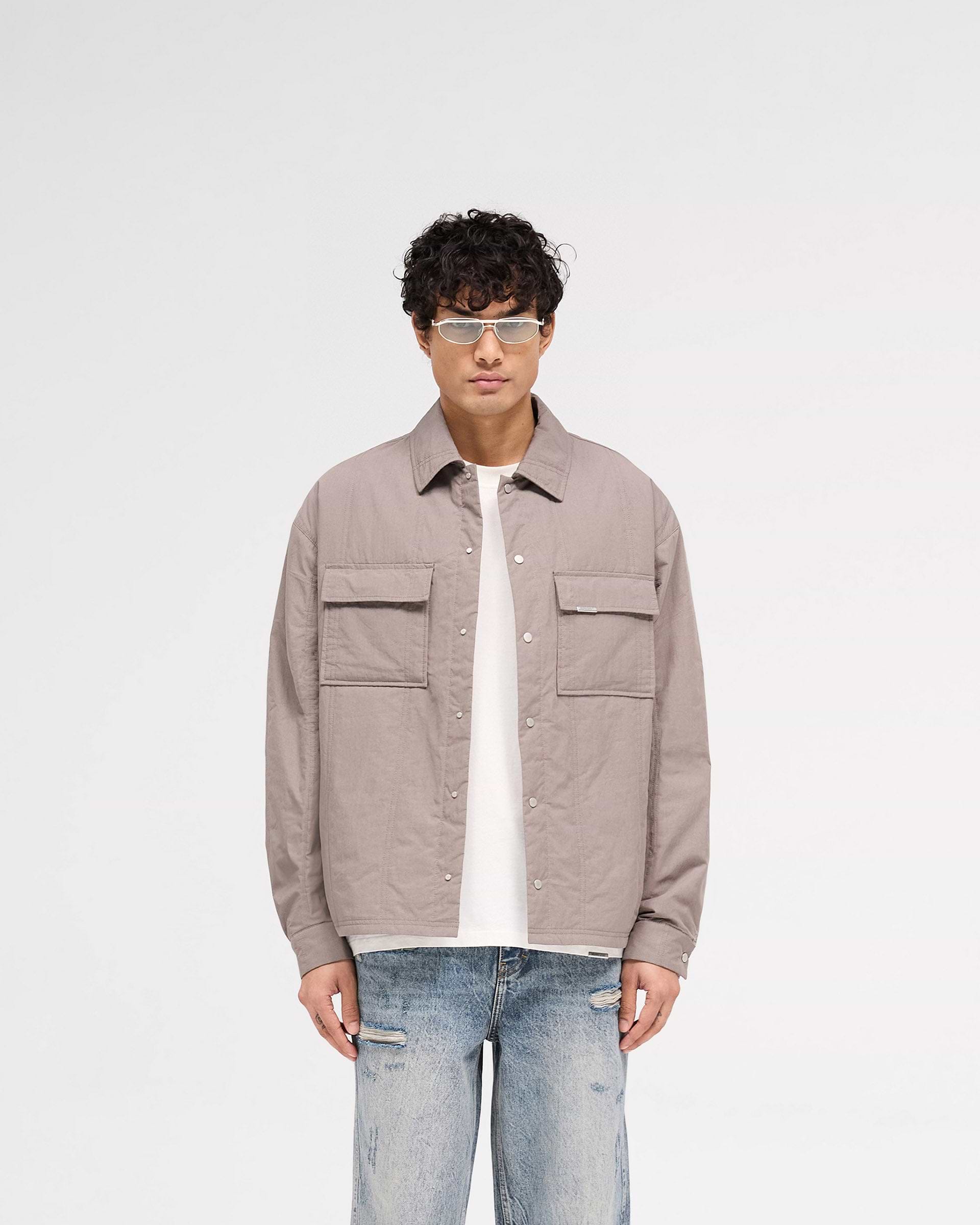 Man wearing a grey quilted overshirt on a plain white background | Quilted Overshirt in Mid Grey | Quilted shirt with light wadding and chest pockets | SS25 Shirts | Represent Clo