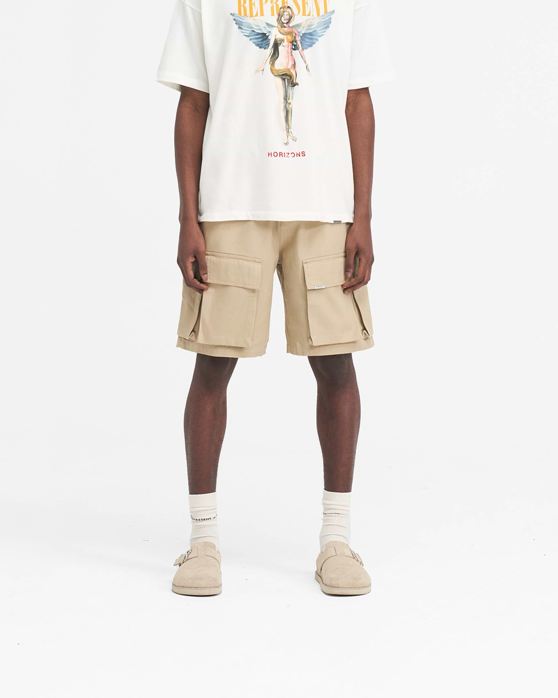 Man wearing a baggy cotton cargo short in sandstone on a plain white background | Baggy Cotton Cargo Short in Sandstone | Baggy fit shorts with 3D oversized pockets | SS24 Shorts | Represent Clo