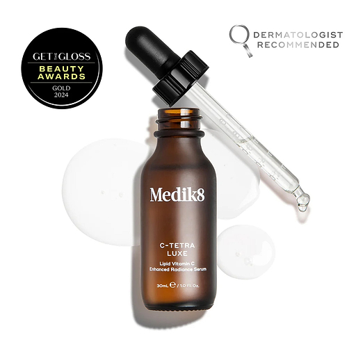Medik8 C-Tetra Luxe serum bottle shown open with its glass pipette resting against the rim, displayed on a white background with clear, translucent serum droplets. The image includes a "GET THE GLOSS BEAUTY AWARDS GOLD 2024" seal in the top left and a "DERMATOLOGIST RECOMMENDED" emblem with a magnifying glass icon in the top right.