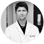 Un portrait d’un scientifique et fondateur Medik8 portant une blouse de laboratoire siglée, représentant la recherche et l’innovation derrière la formulation.