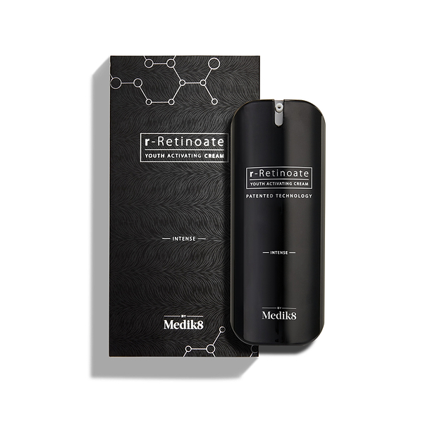 Lahvička Medik8 r-Retinoate Intense Youth Activating Cream stojí vedle své černé vnější krabičky, která obsahuje bílé grafiky chemických hexagonálních struktur a texturovaný vlnitý vzor.
