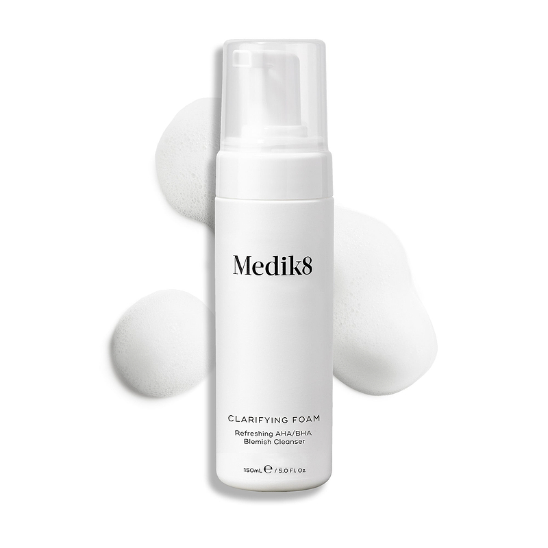 Medik8 Clarifying Foam Pumpflasche auf einem sauberen weißen Hintergrund mit drei Tupfen luftigen weißen Schaums. Text bezeichnet es als Refreshing AHA/BHA Blemish Cleanser in 150 mL Größe