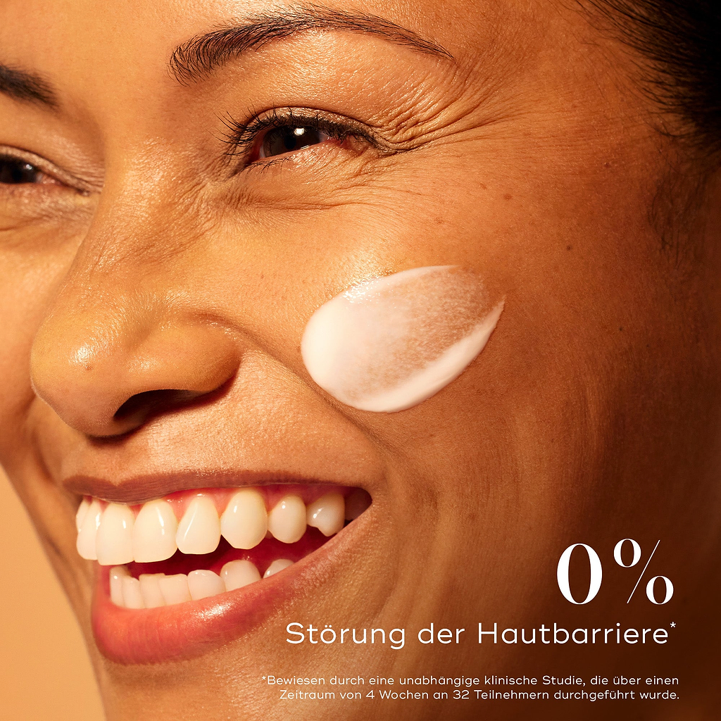 Lächelnde Frau mit strahlender Haut und einem Auftrag des Medik8 C-Tetra Advanced Serums auf der Wange, der 0 % Barrierestörung für sanfte, aber effektive Aufhellung betont.