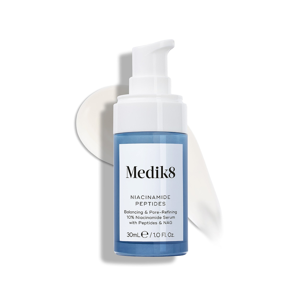 Medik8 Niacinamide Peptides Serumflasche mit weißem Pumpspender, auf einer weißen Oberfläche platziert, mit einem Streifen weißen Serums dahinter.