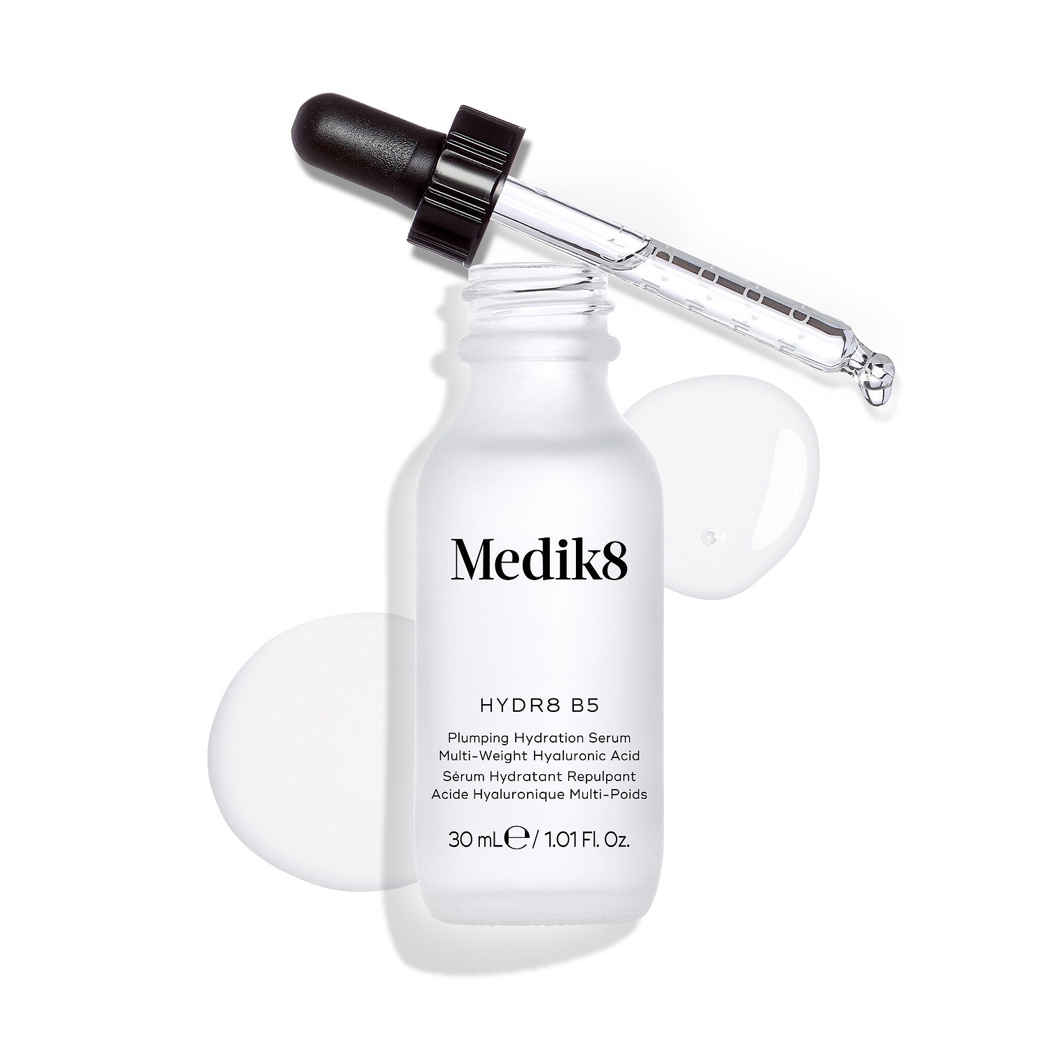 La botella del sérum Medik8 Hydr8 B5 se encuentra sobre un fondo blanco limpio con un charco de líquido transparente y gotas, mientras el cuentagotas descansa en la parte superior. El texto identifica el producto como un “Sérum líquido rehidratante” de 30 mL.