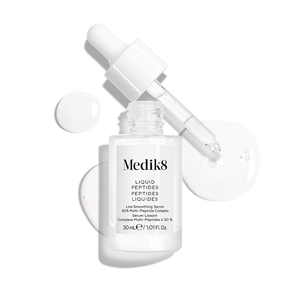 Un frasco cuentagotas de vidrio transparente del sérum Liquid Peptides se presenta con el cuentagotas retirado y colocado al lado, junto a gotas de sérum que muestran la textura del producto.