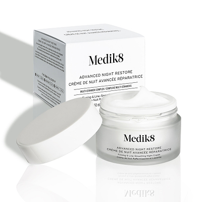 El tarro de crema Advanced Night Restore aparece abierto con su tapa blanca apoyada a un lado y la caja del producto detrás. La imagen muestra la textura rica de la crema y el diseño limpio del envase.