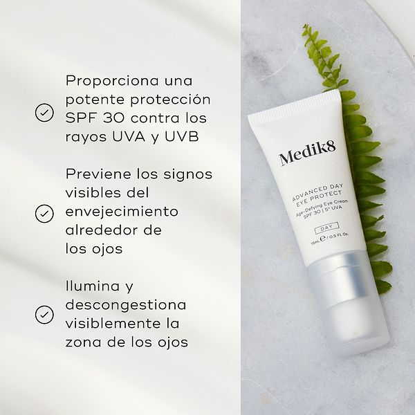 El tubo de Advanced Day Eye Protect yace sobre una superficie de mármol junto a una hoja verde de helecho. El texto destaca su protección SPF 30, la prevención de los signos visibles del envejecimiento y su capacidad para iluminar y desinflamar el contorno de ojos.