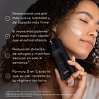 Una persona con cabello rizado sostiene un frasco de Medik8 r-Retinoate Intense Youth Activating Cream junto a su rostro, que tiene una pequeña muestra de la crema color melocotón en la mejilla.