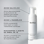 La botella con dispensador de Medik8 Clarifying Foam se encuentra sobre un bloque blanco frente a un fondo gris limpio. El texto destaca los ingredientes clave: Ácido Salicílico para descomponer la acumulación que causa imperfecciones, Ácido L-Mandélico para una exfoliación suave y una tez más clara, y Niacinamida y Aceite de Árbol de Té para ayudar a mantener la piel equilibrada y libre de imperfecciones.