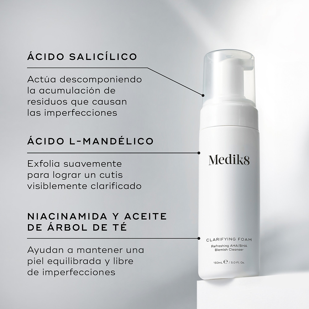 La botella con dispensador de Medik8 Clarifying Foam se encuentra sobre un bloque blanco frente a un fondo gris limpio. El texto destaca los ingredientes clave: Ácido Salicílico para descomponer la acumulación que causa imperfecciones, Ácido L-Mandélico para una exfoliación suave y una tez más clara, y Niacinamida y Aceite de Árbol de Té para ayudar a mantener la piel equilibrada y libre de imperfecciones.