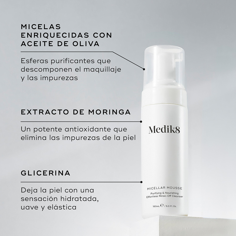 Una botella de Medik8 Micellar Mousse exhibida sobre un bloque blanco. Unas líneas conectan la botella con texto que explica los ingredientes clave: micelas infusionadas con aceite de oliva para descomponer el maquillaje, extracto de moringa para extraer las impurezas y glicerina para proporcionar hidratación.
