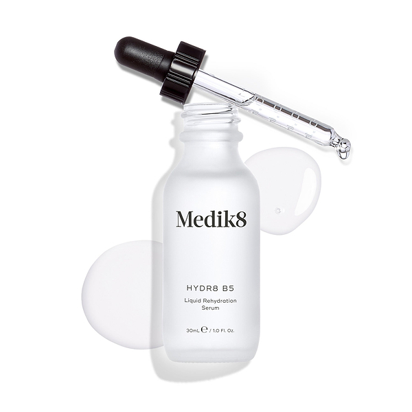 Medik8 Hydr8 B5 serum bottle stands against a clean white background with a clear liquid puddle and droplets, with the dropper resting on top. Text identifies the product as a 30mL "Liquid Rehydration Serum."