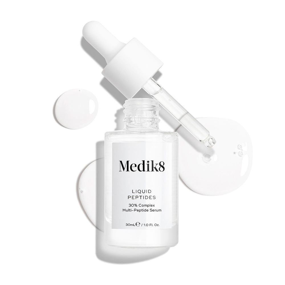 A clear glass dropper bottle of Liquid Peptides serum is presented, with its dropper removed and resting beside it and serum droplets, showing the texture