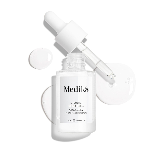 A clear glass dropper bottle of Liquid Peptides serum is presented, with its dropper removed and resting beside it and serum droplets, showing the texture