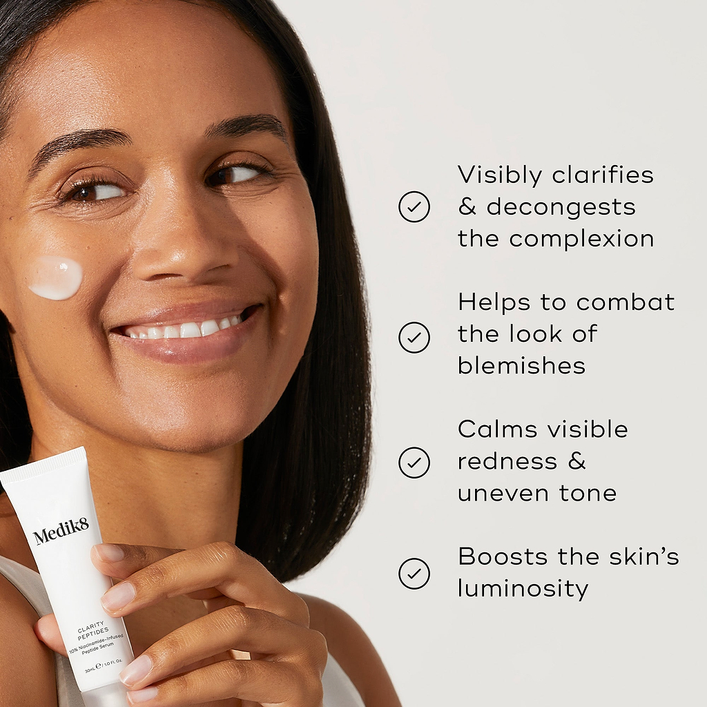 A woman holding Clarity Peptides, with a small amount of product on their cheek. Four bullet points with checkmarks list benefits: Visibly clarifies & decongests the complexion, Helps to combat the look of blemishes, Calms visible redness & uneven tone, and Boosts the skin's luminosity.
