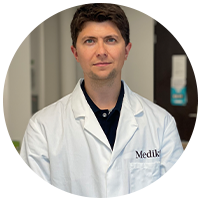A portrait of a Medik8 skincare scientist and founder wearing a branded lab coat, representing the research and innovation behind the formulation.