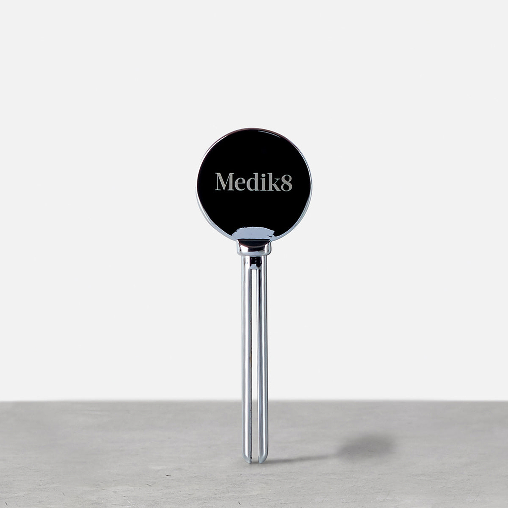 A silver tube squeezer stands upright on a grey surface. 