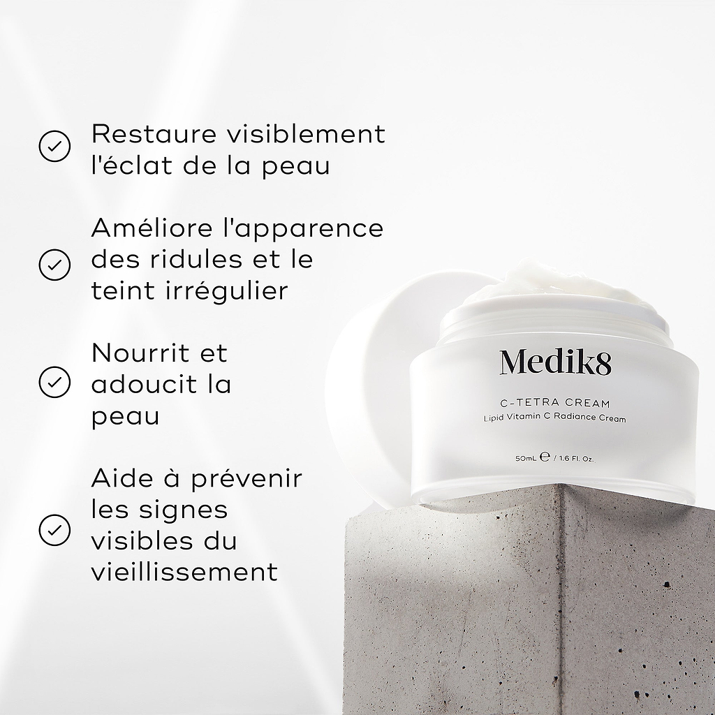 Bocal de crème Medik8 C-Tetra affiché sur un bloc de pierre grise sur fond blanc avec des rayons de lumière douce. L’image présente quatre affirmations avec coche : Restaure visiblement l’éclat de la peau, Améliore l’apparence des ridules et du teint irrégulier, Nourrit et adoucit la peau, Aide à prévenir les signes visibles du vieillissement
