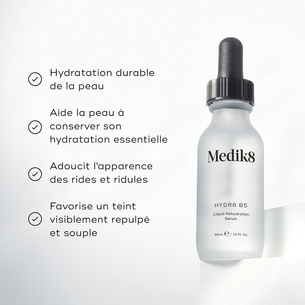 Le flacon de sérum Medik8 Hydr8 B5 est placé sur un socle blanc devant un fond blanc lumineux. Le texte met en avant que le produit « apporte une hydratation longue durée », « aide la peau à retenir l’humidité essentielle », « adoucie l’apparence des ridules et des rides » et « favorise un teint visiblement repulpé et souple ».