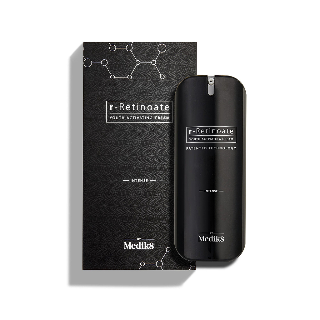 Le flacon de Medik8 r-Retinoate Intense Youth Activating Cream est placé à côté de son emballage extérieur noir, avec des graphiques hexagonaux chimiques blancs et un motif ondulé texturé 