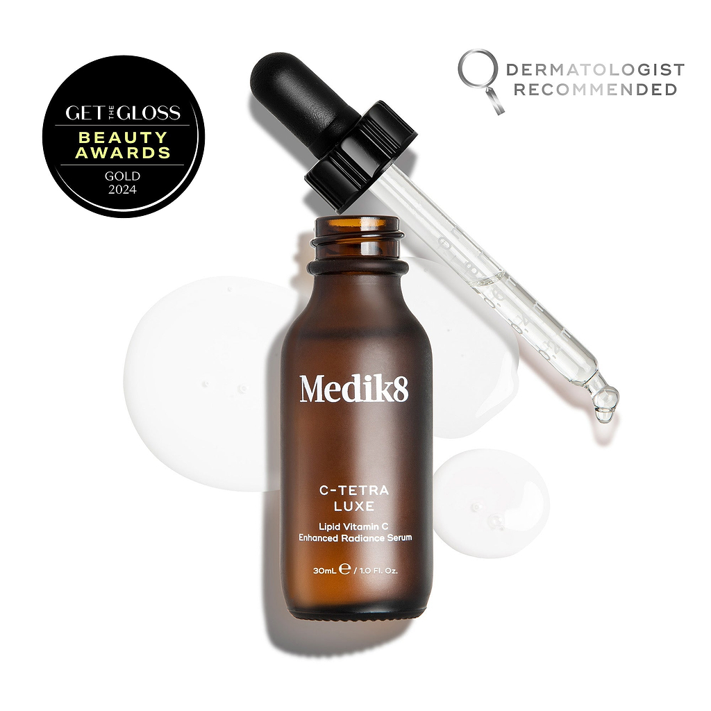Flacon de sérum Medik8 C-Tetra Luxe ouvert avec sa pipette en verre reposant sur le rebord, présenté sur un fond blanc avec des gouttelettes de sérum translucides. L'image inclut un sceau GET THE GLOSS BEAUTY AWARDS GOLD 2024 en haut à gauche et un emblème DERMATOLOGIST RECOMMENDED avec icône loupe en haut à droite