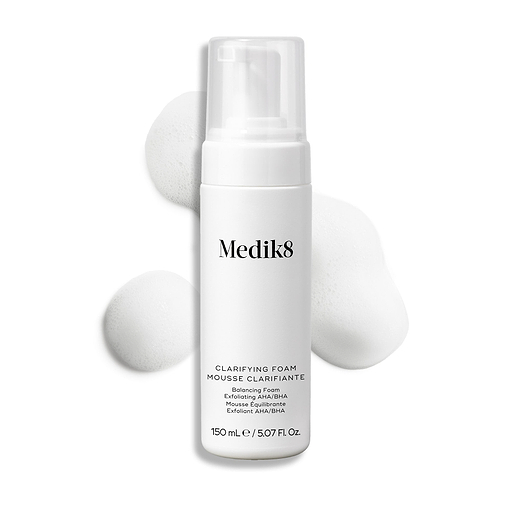Flacon-pompe Medik8 Clarifying Foam présenté sur un fond blanc propre avec trois petites touffes de mousse blanche aérienne. Le texte l'identifie comme un Refreshing AHA/BHA Blemish Cleanser de 150 mL