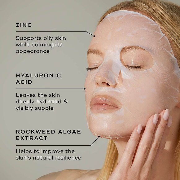 Close-up of a person wearing a translucent white sheet mask on their face against a light grey background. Text points to key ingredients: ZINC (Supports oily skin while calming its appearance), HYALURONIC ACID (Leaves the skin deeply hydrated & visibly supple), and ROCKWEED ALGAE EXTRACT (Helps to improve the skin's natural resilience).-hover-39
