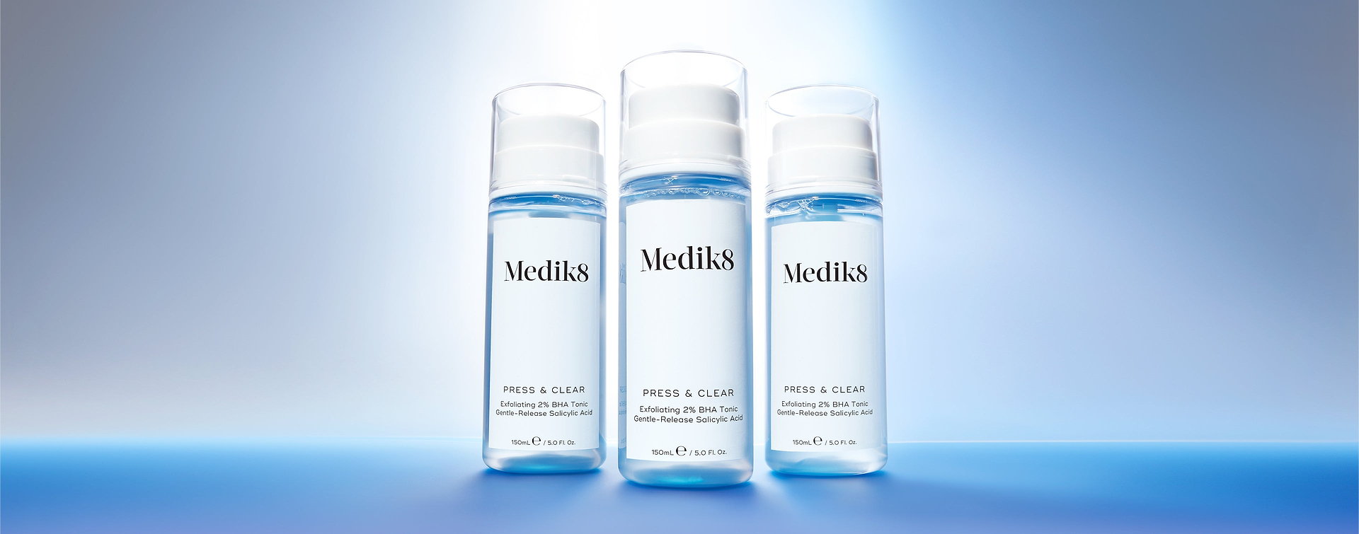 Tři lahvičky Medik8 Press & Clear Exfoliating 2% BHA Tonic na zářivě modrém přechodovém pozadí.