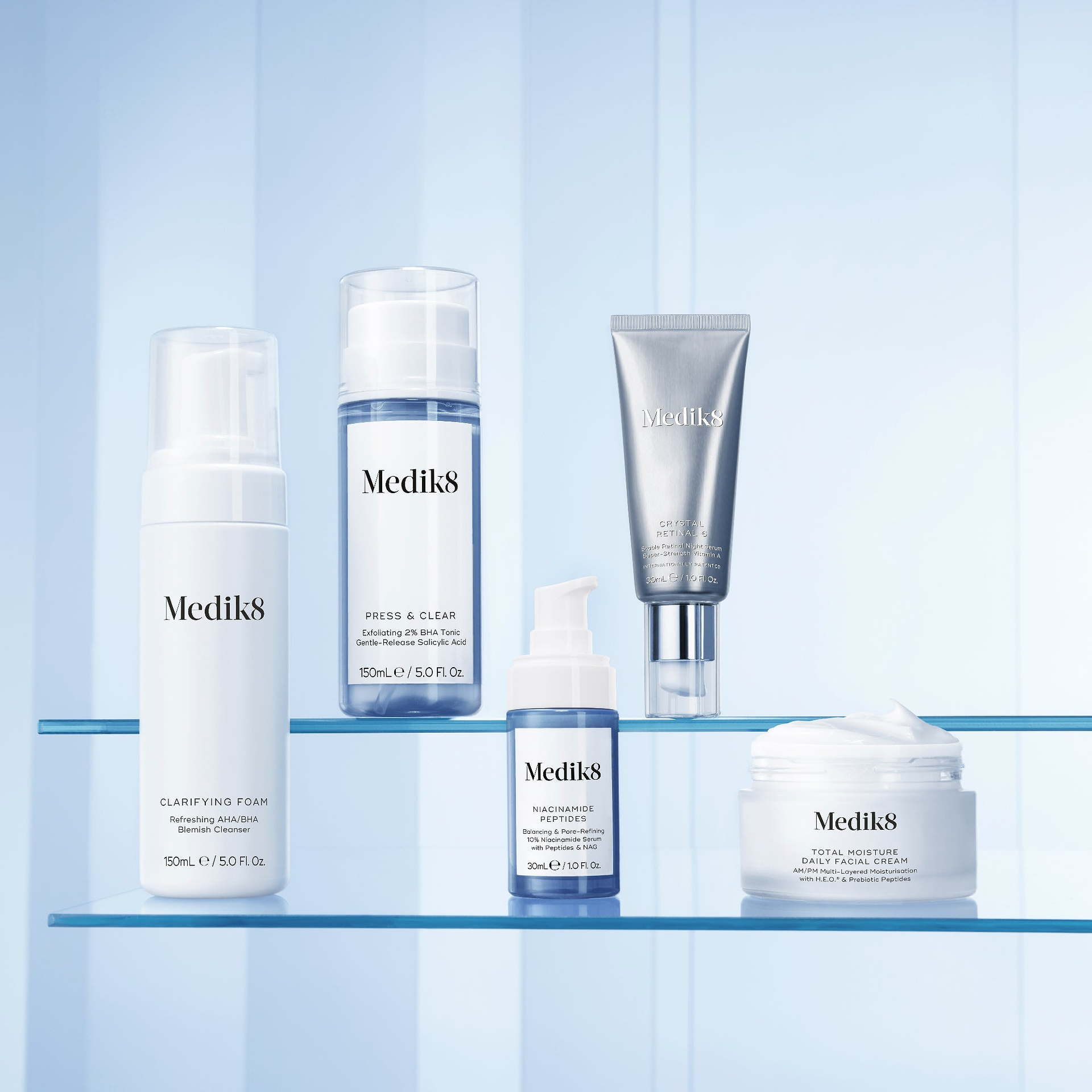 Čisticí pěna Medik8 Clarifying Foam, Press & Clear, Niacinamide Peptides, Crystal Retinal 6 a krém Total Moisture Cream na skleněných poličkách.