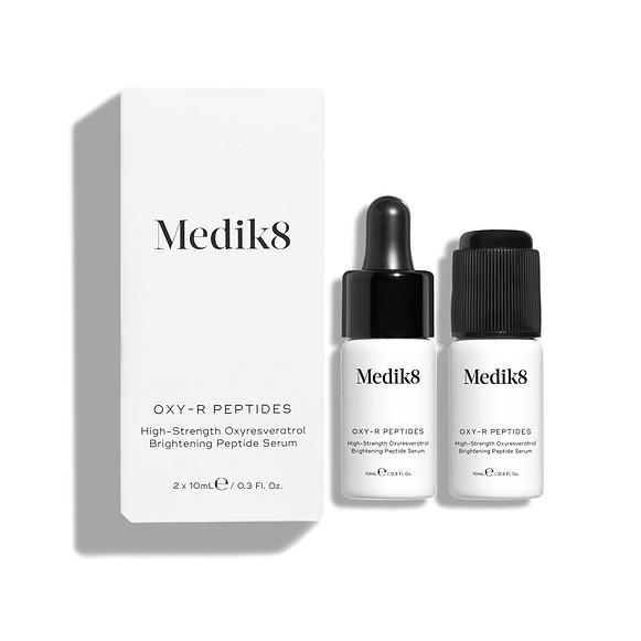 Eine weiße Produktverpackung des Medik8 Oxy-R Peptides steht neben zwei kleinen weißen Flaschen des Serums. Eine Flasche hat einen schwarzen Tropfer, die andere einen schwarzen Verschluss.-7