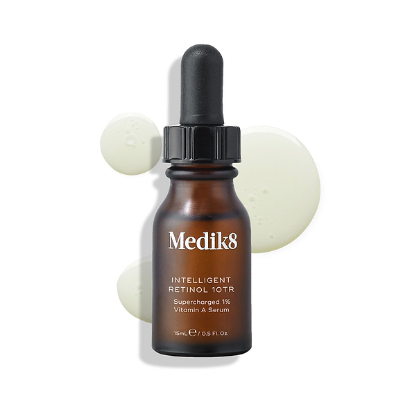 A brown glass dropper bottle of Medik8 Intelligent Retinol 10TR is displayed, with three pale yellow serum droplets on the white surface. -6